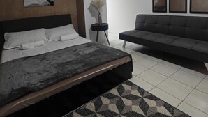 Un dormitorio con una cama, un sofá, un cuadro y un jarrón con flores secas.