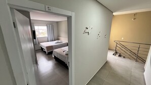 A hotel room with two beds, a window with curtains, a staircase, and a wall-mounted light fixture. - PENHA SOLAR INN (Centro Penha)