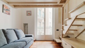 Una sala de estar moderna con un sofá, una escalera de madera y una puerta que da a un balcón exterior.