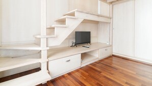 Una habitación con escalera de madera, televisor de pantalla plana y piso de madera.