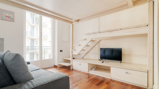 Una sala de estar moderna con sofá, televisión, estanterías de madera y una escalera.