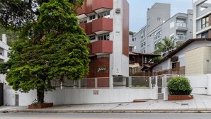 Un edificio moderno con fachada roja y blanca, entrada protegida por una reja y un gran árbol en primer plano.