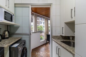 Een kleine keuken met een magnetron, wasmachine en granieten aanrechtbladen.