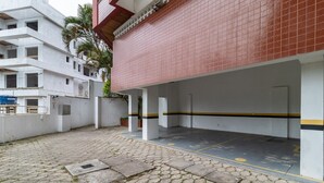 Un área de estacionamiento techada con un muro de tejas rojas y un edificio blanco al fondo.