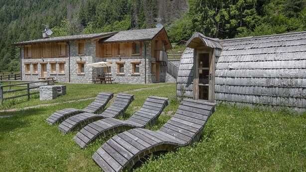 A rustic lodge with stone walls and wooden beams, featuring a wooden deck with lounge chairs and a picnic table.