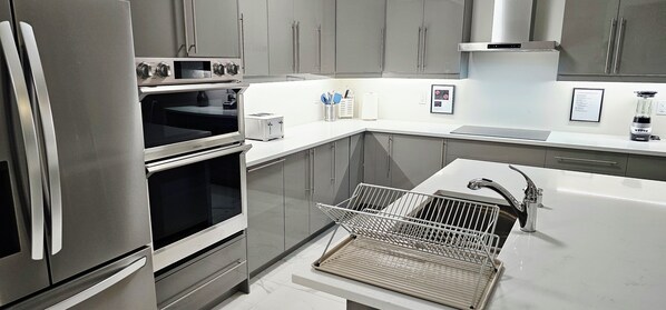 A modern kitchen with stainless steel appliances, a built-in oven, a dishwasher, and a sink with a dish rack.