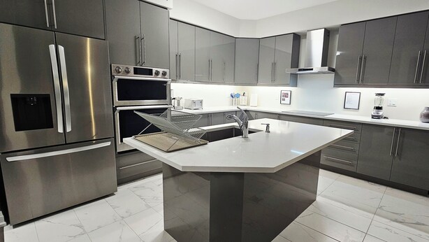 A modern kitchen with stainless steel appliances, a central island, and grey cabinetry.