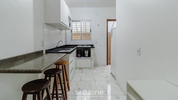 A modern kitchen with white cabinets, a granite countertop, and a built-in stove. There are three wooden stools and a small coffee machine. - Apt Just Minutes From Lagoa da Conceicao - Sis0005 (Florianópolis)