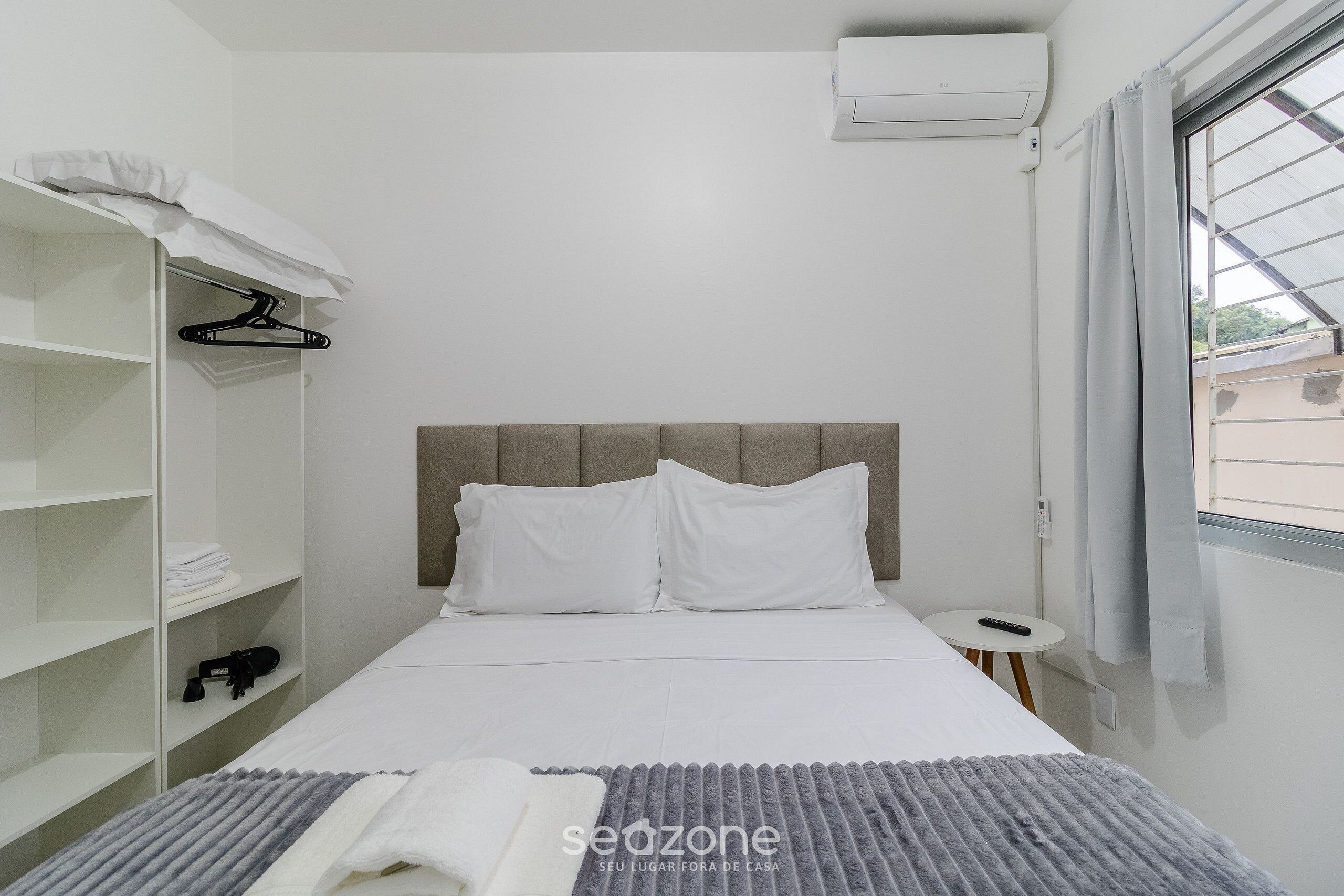 A neatly arranged hotel room with a bed, a wardrobe, a small table, and a window with curtains.
