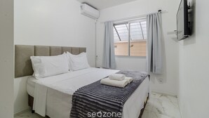 A bedroom with a bed, a flat-screen TV, an air conditioner, and a window with curtains. - Apt Just Minutes From Lagoa da Conceicao - Sis0005 (Florianópolis)
