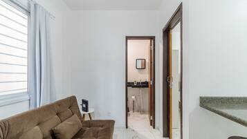 Sala de estar com sofá, uma pequena mesa lateral e cozinha visível através de uma porta aberta.