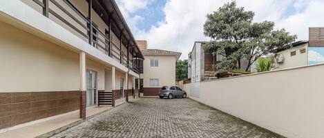 Un patio empedrado con un coche estacionado al fondo, rodeado de edificios con balcones y un árbol.