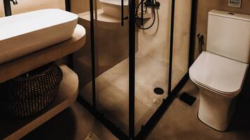 Un baño moderno con ducha de vidrio, un lavabo blanco y un inodoro.