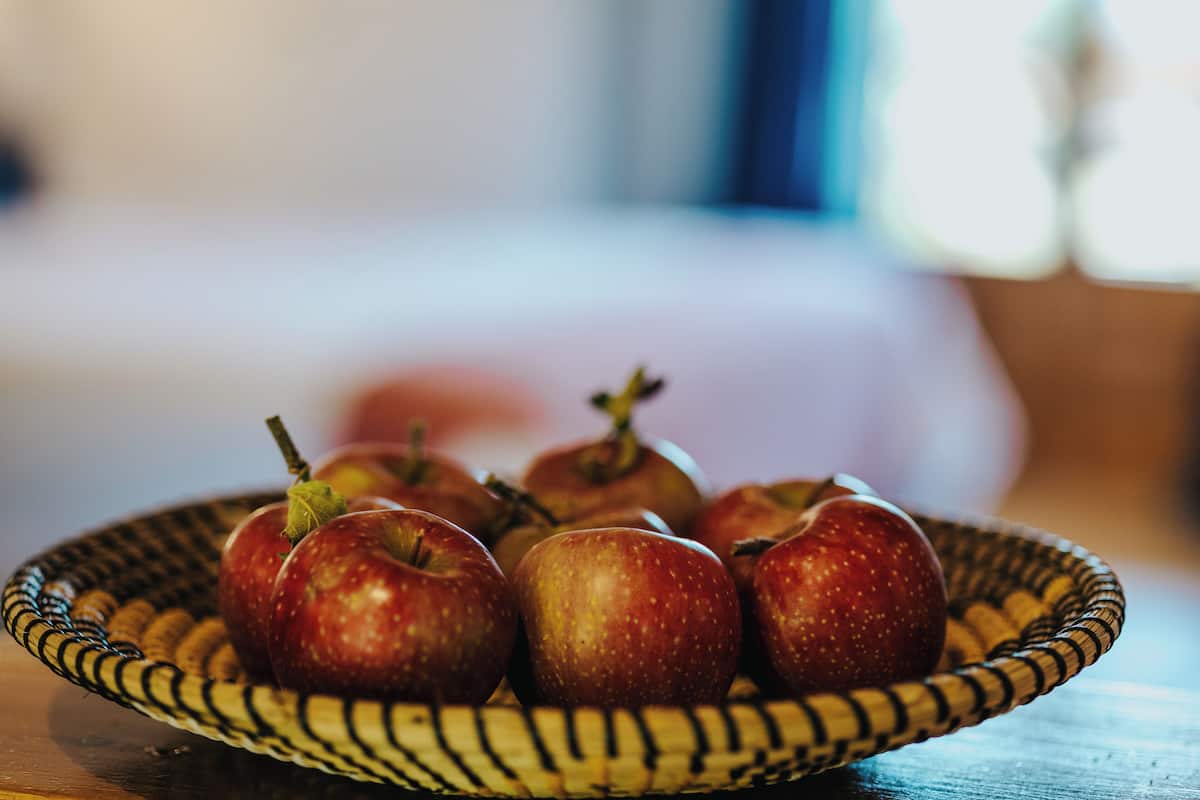 A wicker bowl containing several apples on a wooden surface.