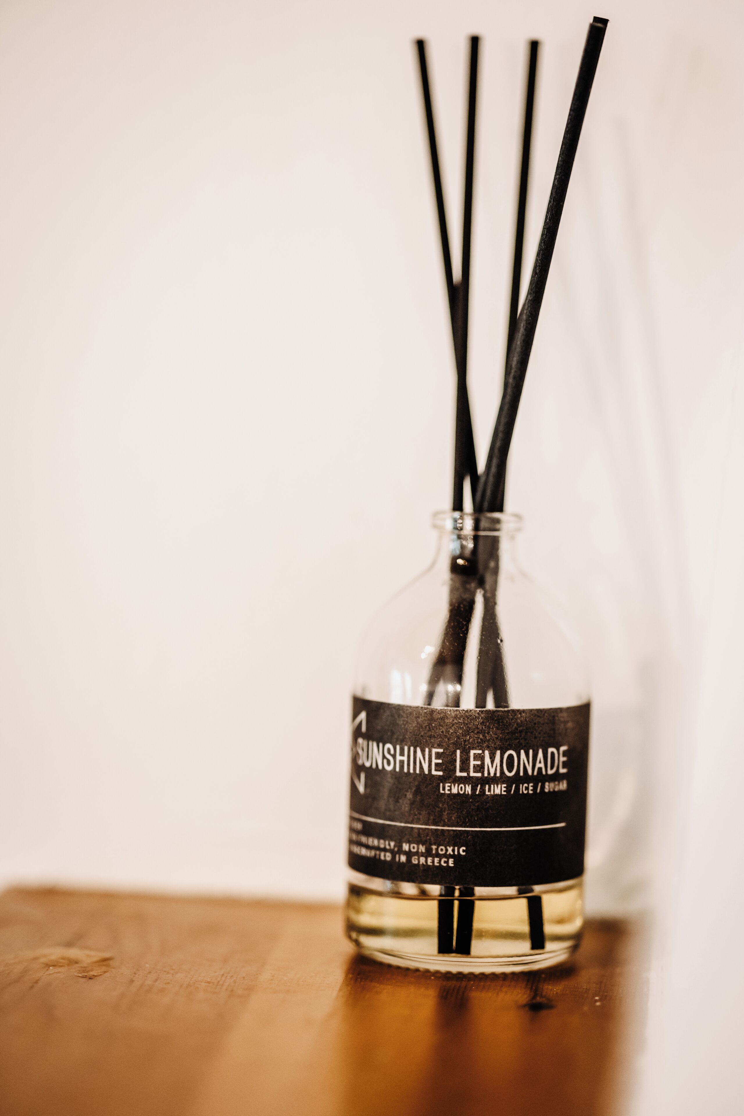 Uma garrafa de limonada Sunshine Lemonade com palitos pretos, identificada como não tóxica e produzida na Grécia, sobre uma superfície de madeira.