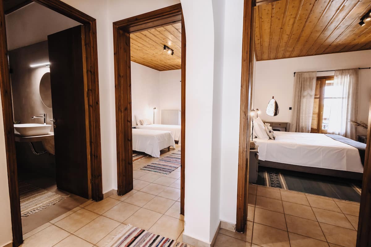 A hotel room with two beds, a bathroom with a sink, and a wooden ceiling.