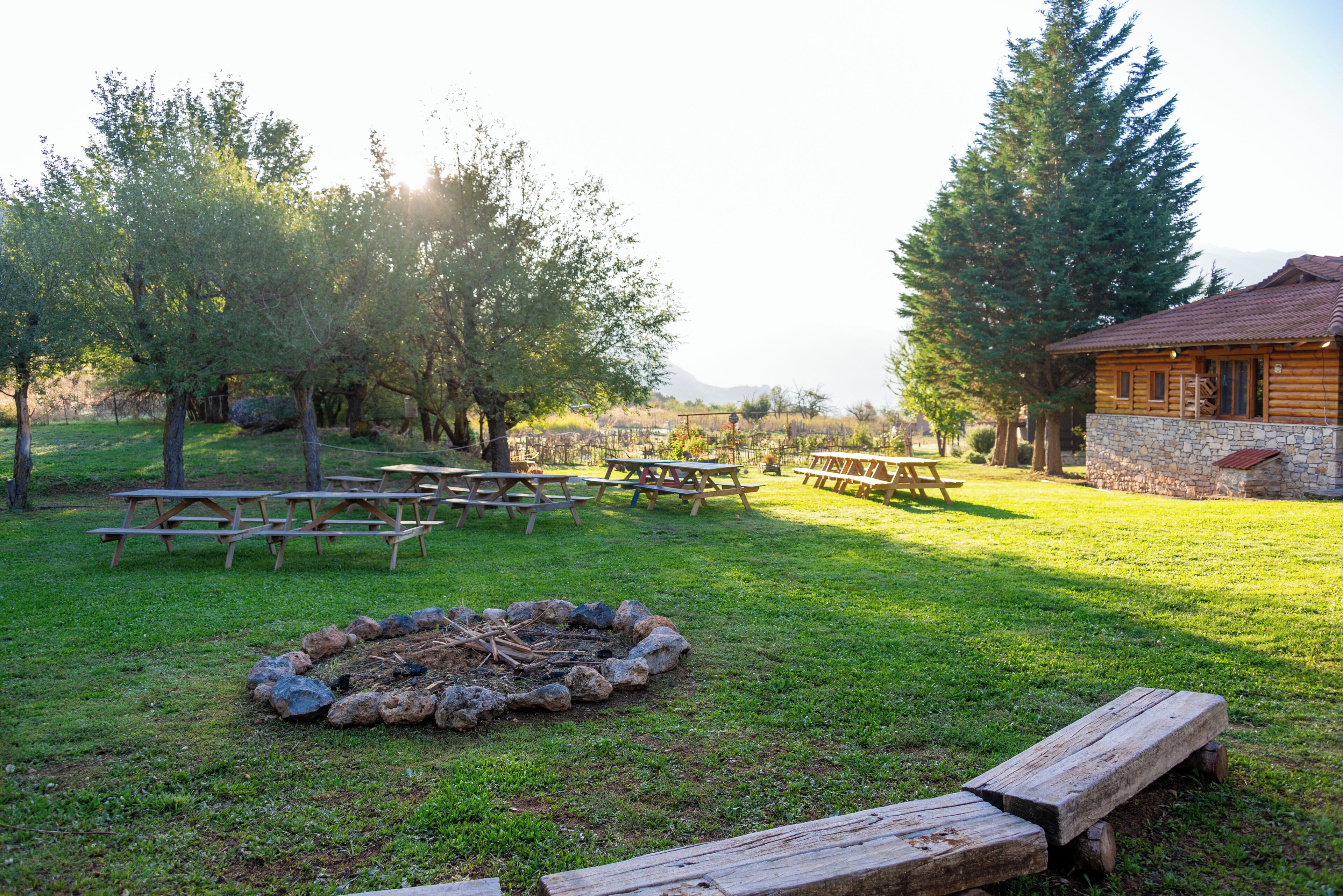 A rustic outdoor setting with picnic tables, a fire pit, and a stone cabin.