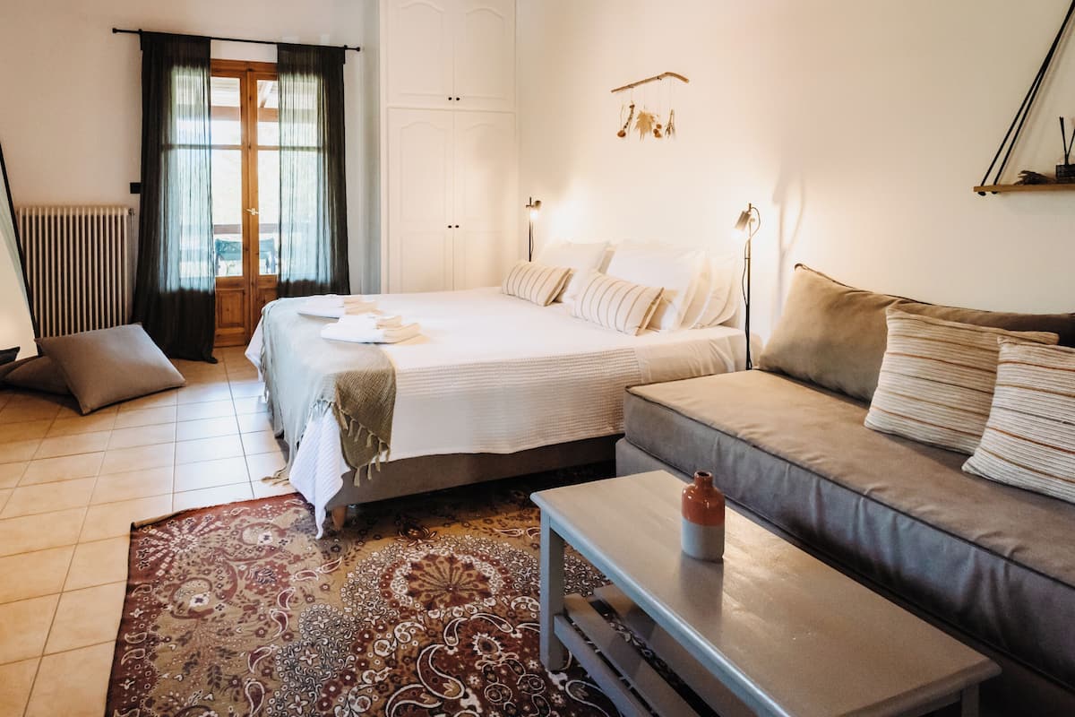 A hotel room with a bed, a sofa, a table, a chair, a TV, and a window with curtains.