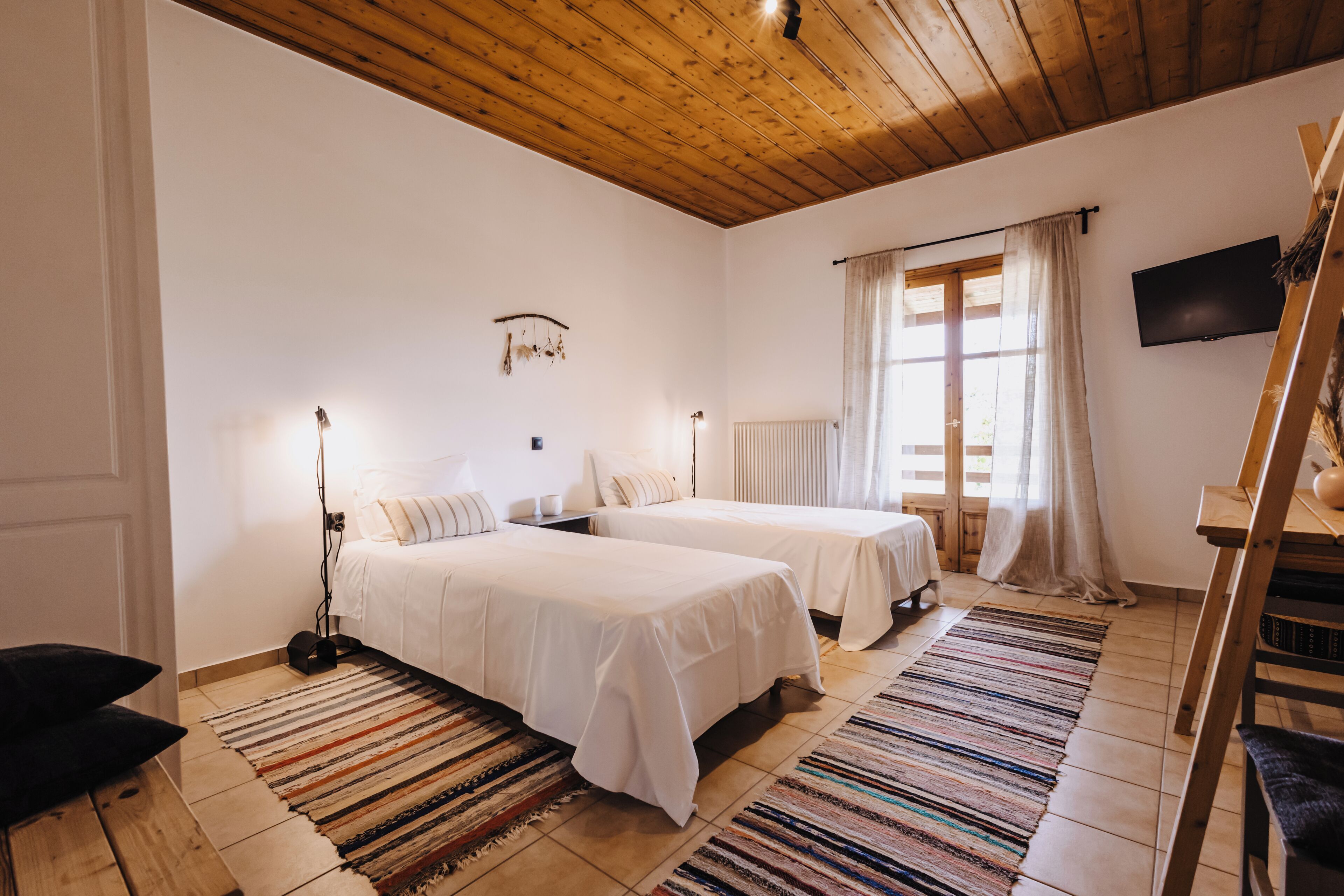 Habitació amb dos llits, sostre de fusta, televisió i finestra amb cortines.