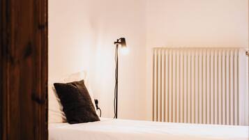 A bedroom with two beds, a bedside lamp, a radiator, and a wooden door.