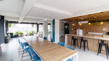 A modern office space with a long wooden table, blue chairs, a bar area with stools, and a view of the outside.