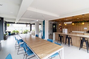 Een moderne kantoorruimte met een lange houten tafel, blauwe stoelen, een bar met krukken en uitzicht op buiten.