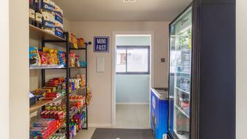 Un pasillo con estantes llenos de aperitivos y bebidas, un letrero de comida rápida y un refrigerador.