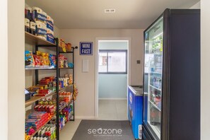 Un pasillo con estantes llenos de aperitivos y bebidas, un letrero de comida rápida y un refrigerador.
