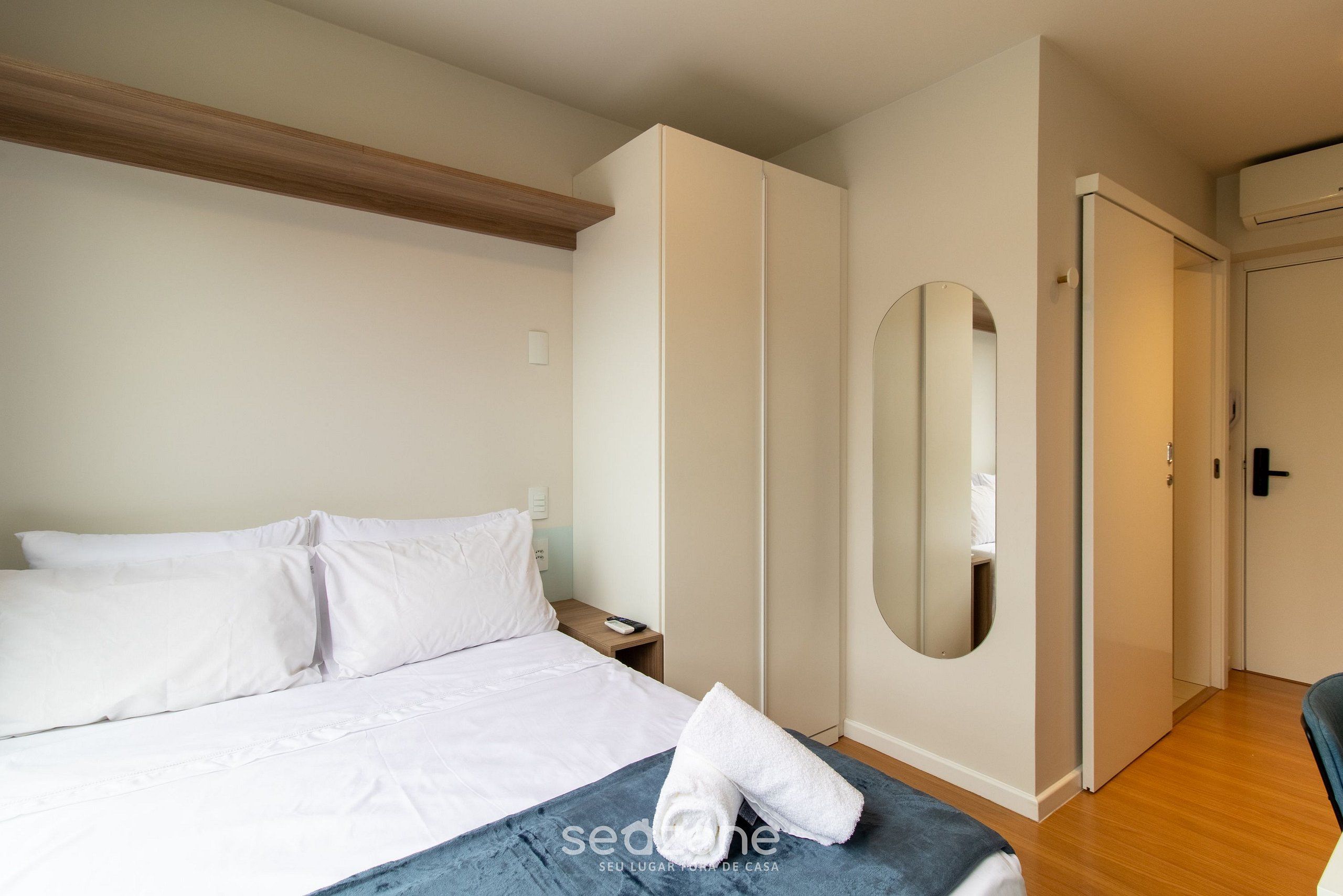 A hotel room with a bed, a nightstand, a mirror, and a wardrobe.
