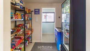 A hallway with shelves stocked with snacks and beverages, a mini fast food sign, and a refrigerator. - Modern Studio Just Minutes From the Beach Sid0209 (Florianópolis)