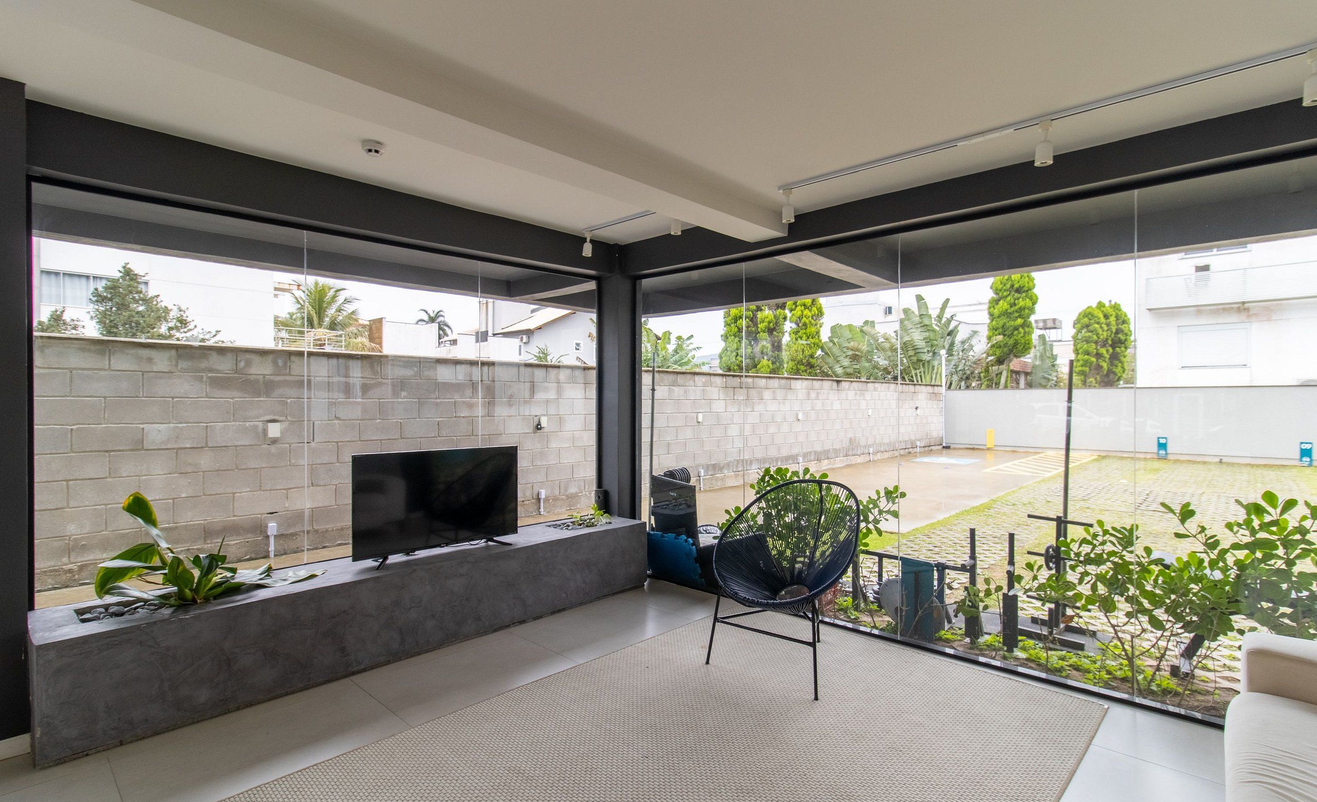 A modern living room with a flat-screen TV on a built-in shelf, a black chair, and a view of the backyard through large windows.