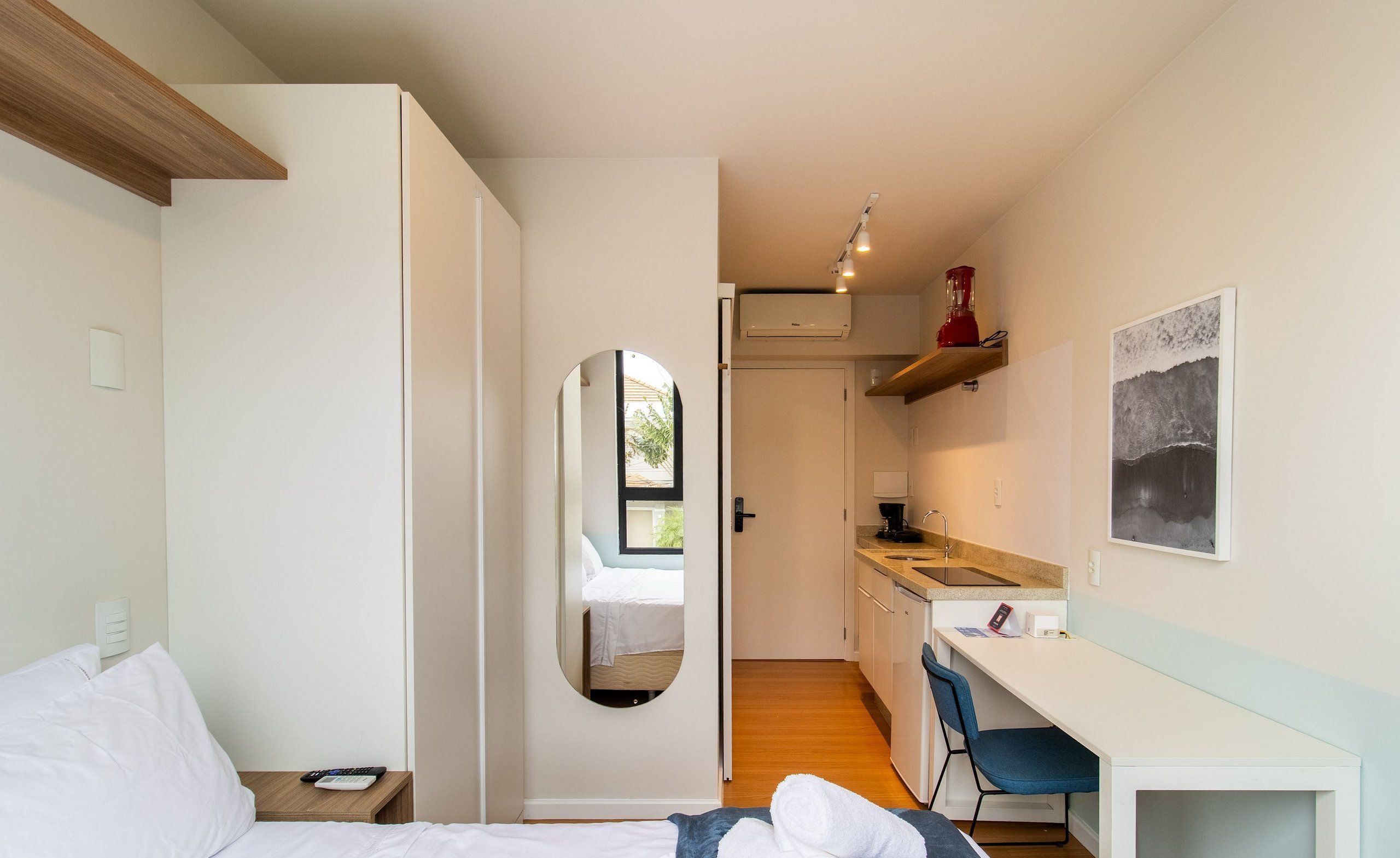 A bedroom with a bed, a desk, a chair, and a small kitchen area.