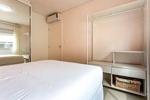 Una habitación de hotel con una cama, un armario, una estantería con una cesta y un equipo de aire acondicionado.