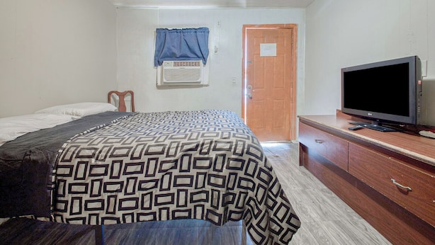 A bedroom with a bed, a television on a wooden dresser, and a door.