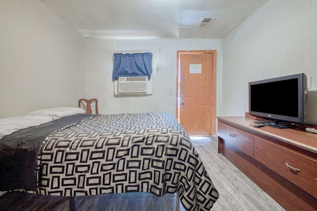 A bedroom with a bed, a television on a wooden dresser, and a door.
