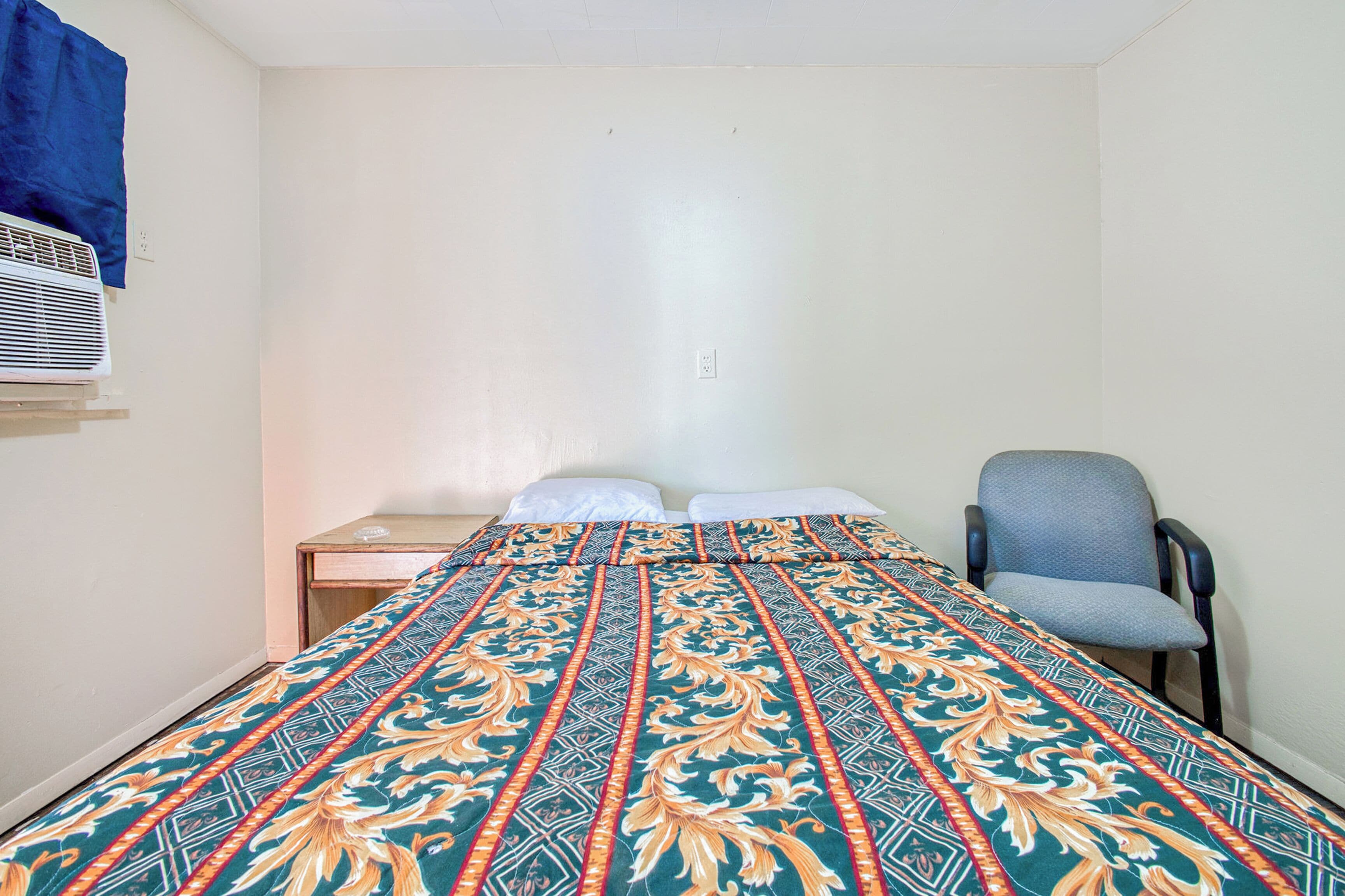 A small, simple room with a bed, a chair, and a desk.