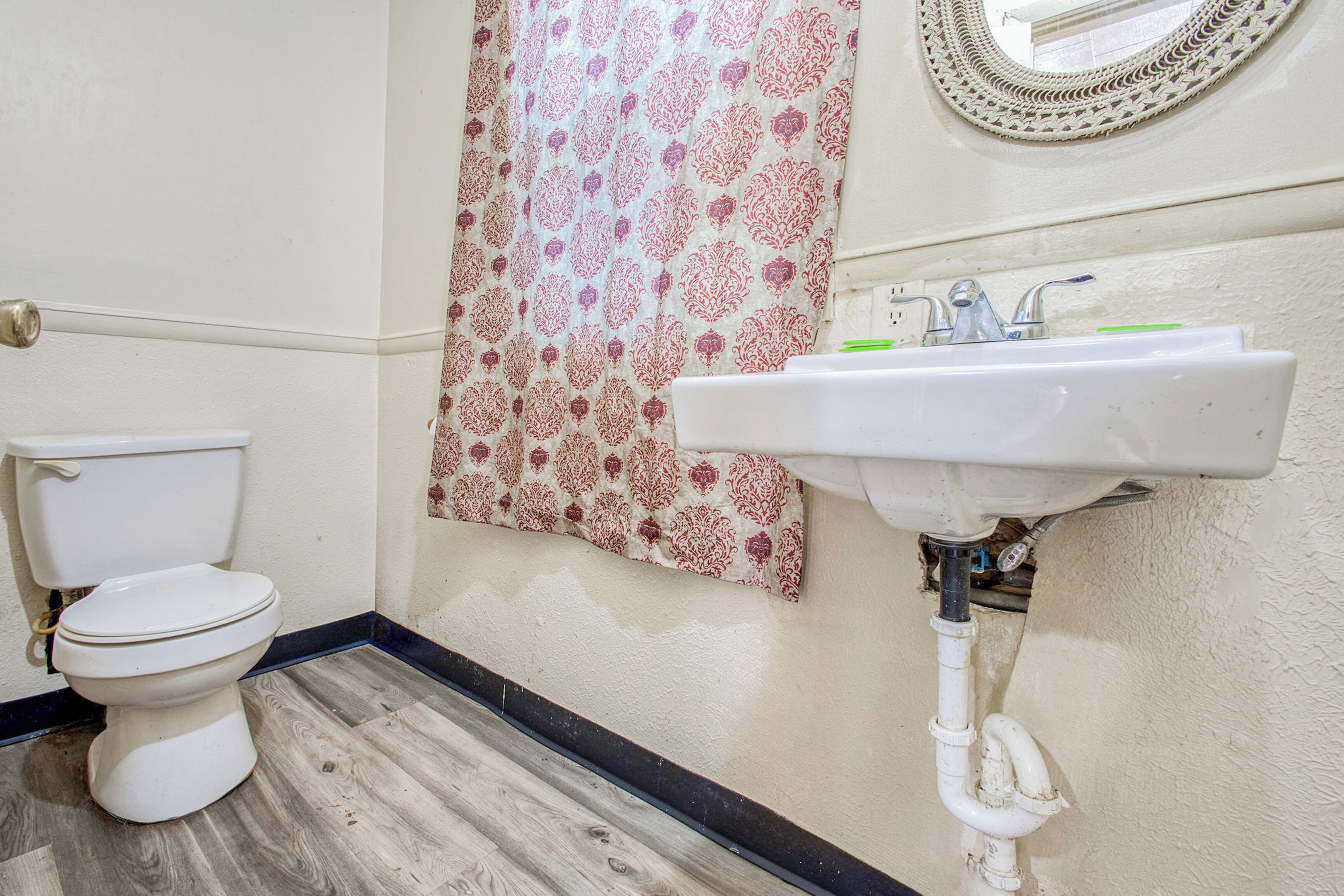 Un baño con inodoro, lavamanos, cortina de ducha estampada y espejo con marco decorativo.