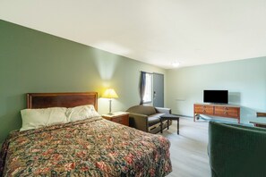 Une chambre d’hôtel avec un lit, une chaise, une télévision, une commode et une lampe.