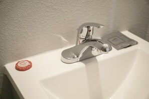 Un lavabo blanc pour la salle de bain, doté d’un robinet chromé et d’un distributeur de savon.