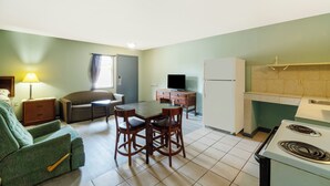A compact living space with a dining table, chairs, a sofa, a television, a refrigerator, and a kitchen area with a stove. - Capital O Parker Motel Clute Jackson Tx 332 (Clute)