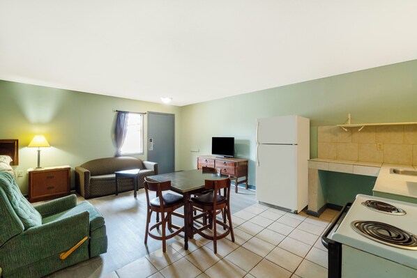A compact living space with a dining table, chairs, a sofa, a television, a refrigerator, and a kitchen area with a stove. - Capital O Parker Motel Clute Jackson Tx 332 (Clute)