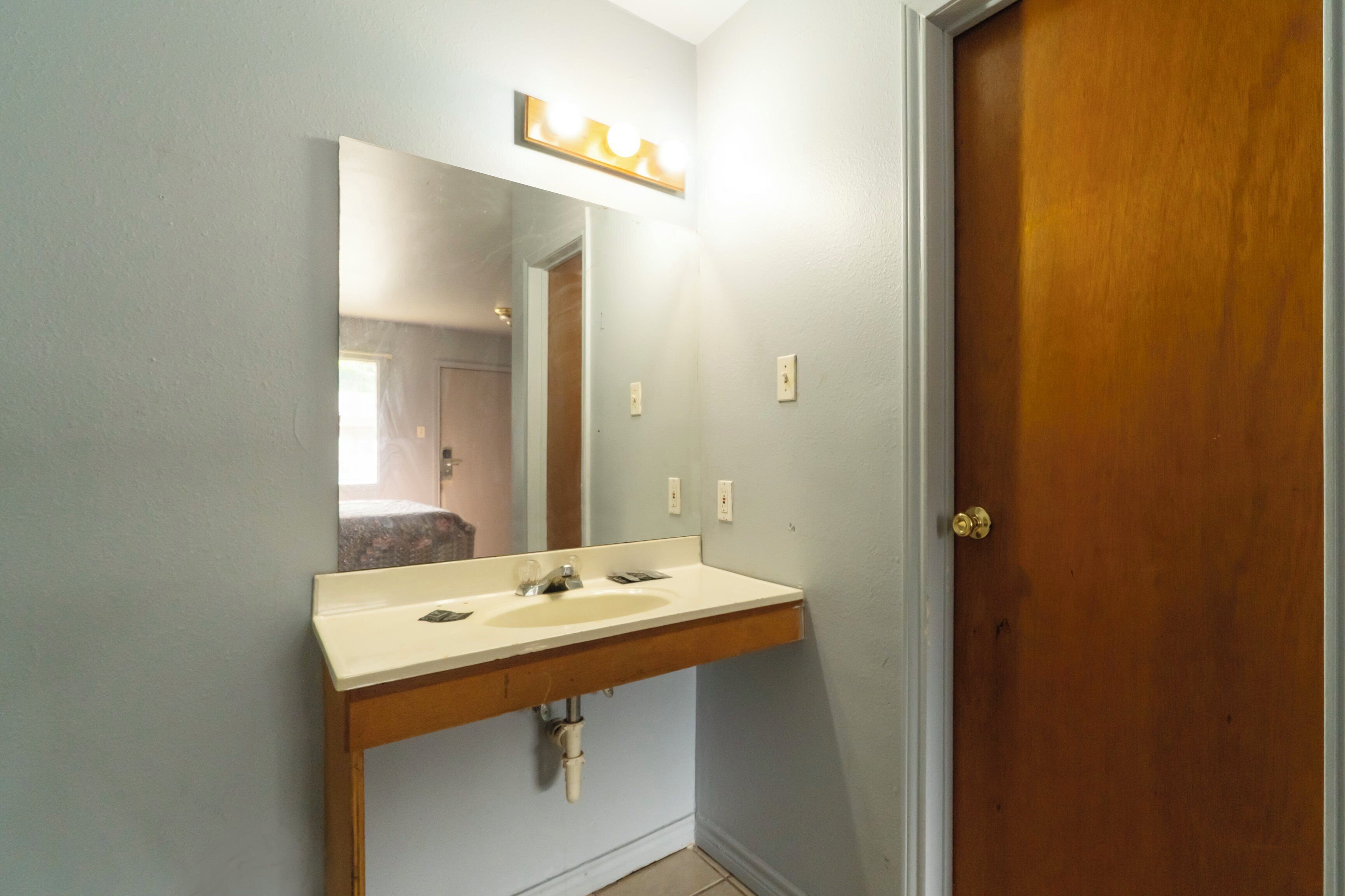 A bathroom with a wooden vanity, a mirror with lights, and a wooden door.