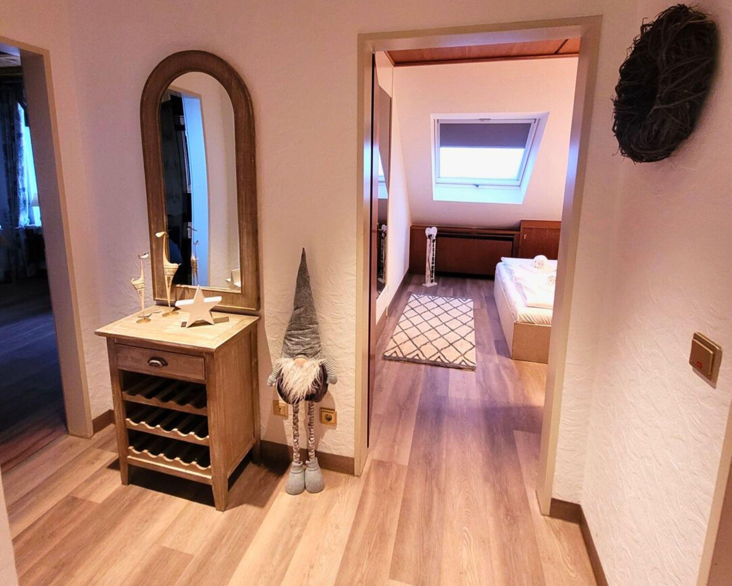 Un pasillo con un tocador de madera, una decoración de gnomo, un tragaluz y un dormitorio con cama y ventana.