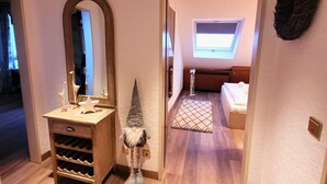 A hallway with a wooden vanity, a gnome decoration, a skylight, and a bedroom with a bed and a window. - Apartment With Covered Balcony (Winterberg)