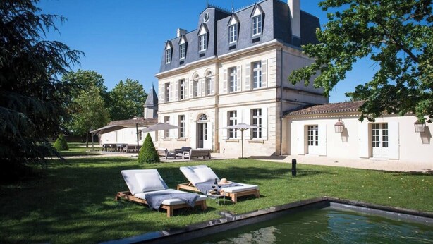 A large, historic building with a symmetrical facade, a central entrance, and a well-maintained lawn with two sun loungers and a small pool.