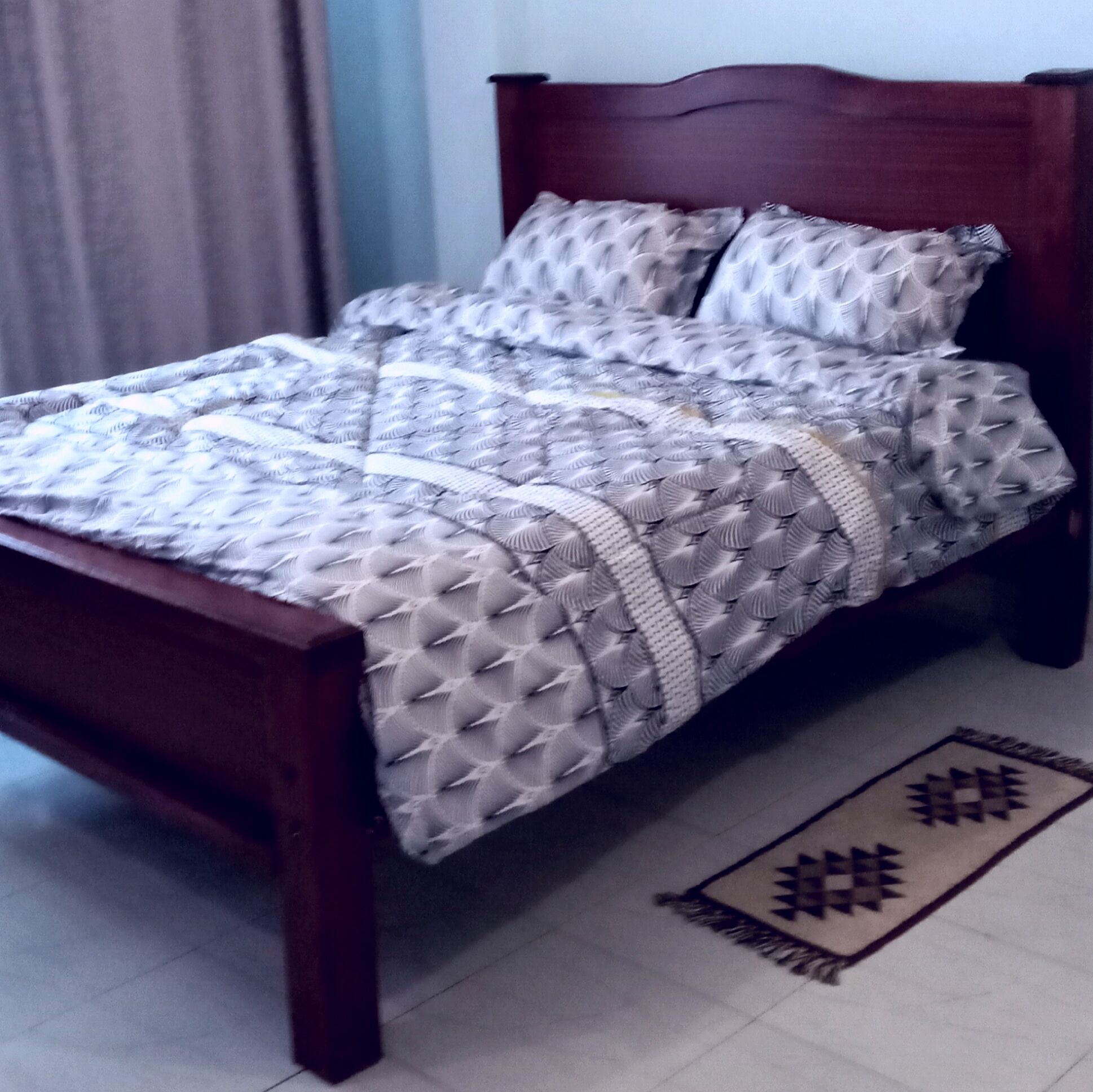 A bed with a patterned bedspread and pillows, a wooden headboard, and a rug with a geometric design on the floor.