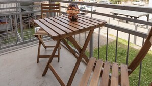 Un balcón con mesa y sillas de madera, barandilla de metal y vista a una calle con edificios y coches.