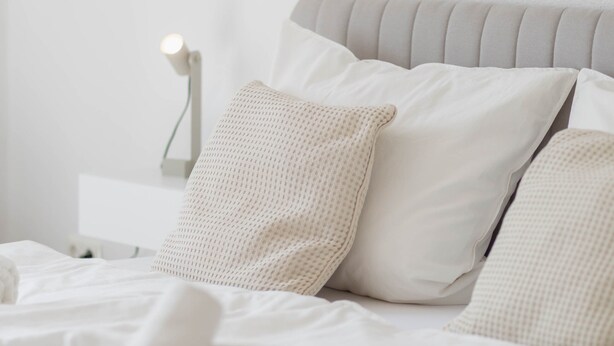 Una cama bien hecha con almohadas y una lámpara de noche.