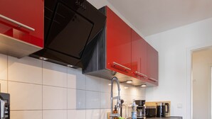 Una cocina moderna con armarios rojos, una campana extractora negra, un lavamanos de acero inoxidable y un microondas.