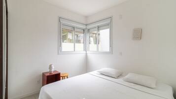Un dormitorio con una cama, una mesita de noche pequeña y un ventanal.